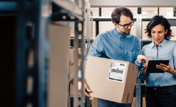 Customers in warehouse with a box looking at a tablet.